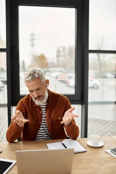 Ein älterer Mitarbeiter gestikuliert nachdenklich, während er im sonnigen Büro über Arbeitsangelegenheiten diskutiert. — Stockfoto