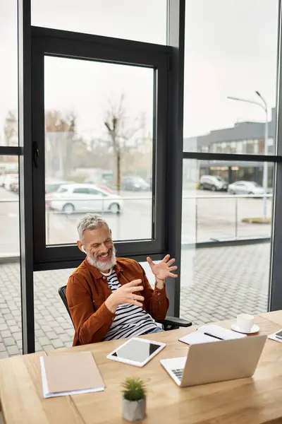 Un uomo barbuto grigio discute entusiasticamente le idee mentre è seduto in un ufficio elegante. — Foto stock