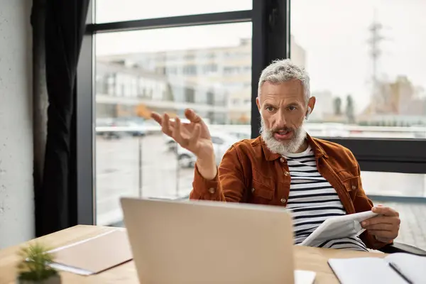 A man passionately expresses his thoughts while seated at a modern desk, surrounded by paperwork. — Stock Photo