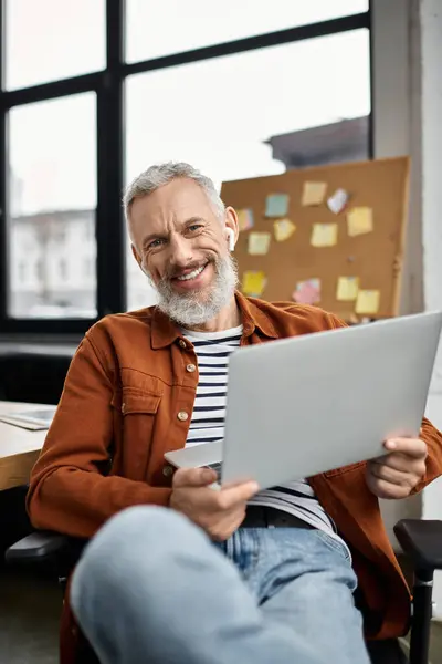Un professionnel souriant s'engage avec un ordinateur portable tout en étant assis confortablement dans un cadre de bureau élégant. — Photo de stock