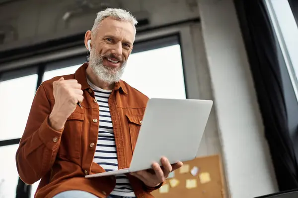 A man celebrates a work win at a bright office with natural light, using his laptop. — Stock Photo