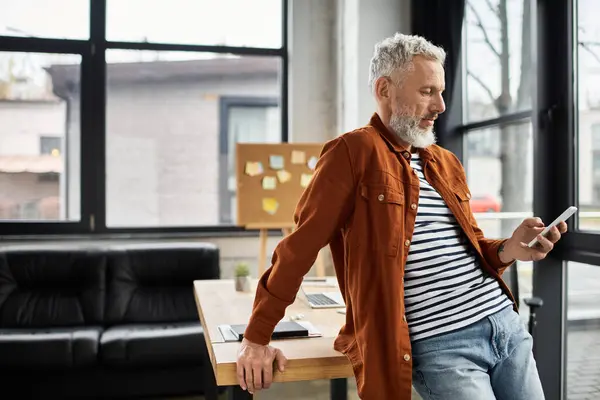 Individual in stylish attire interacts with a smartphone while relaxing in a bright office space. — Stock Photo