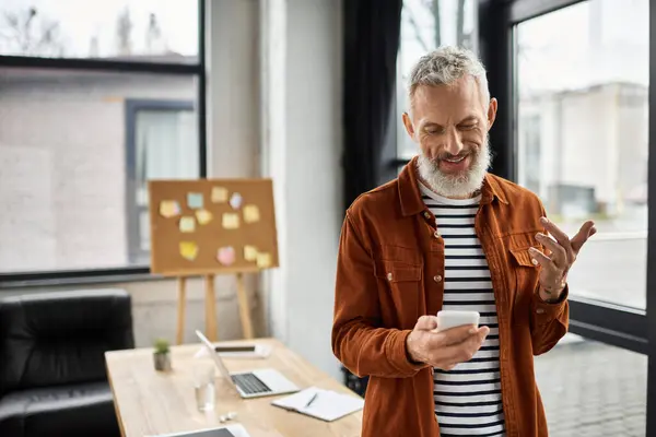 In a stylish office, a man enjoys a moment while looking at his smartphone, smiling and engaged. — Stock Photo