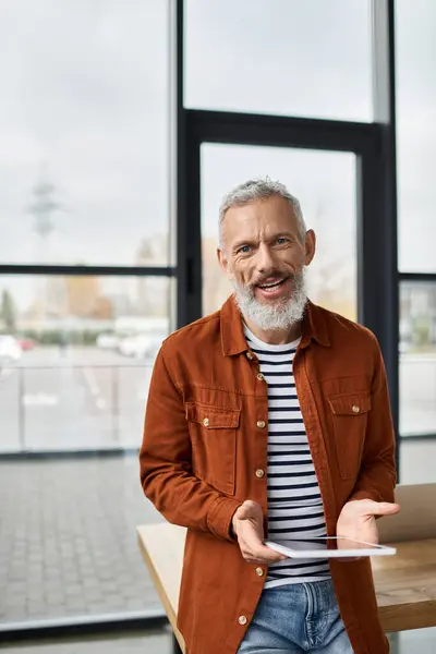 Homme âgé avec une expression heureuse se tient dans le bureau contemporain tenant une tablette pendant le travail. — Photo de stock