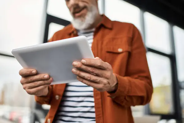 An elderly man with a beard interacts with a tablet while standing in a contemporary office space. — Stock Photo