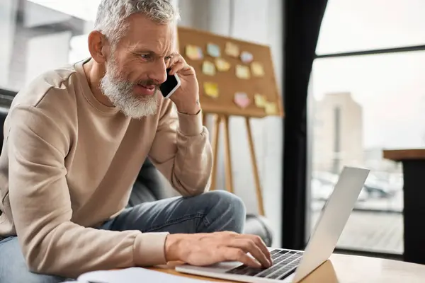 A professional man makes a call while working on his laptop in a sleek workspace. — Stock Photo