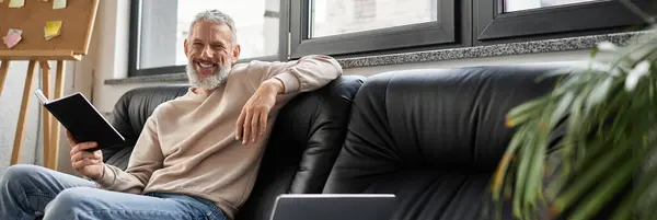 Cozy office corner with a relaxed man reading a notebook amidst greenery and sunlight. — Stock Photo