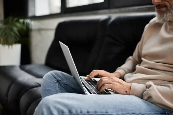 A person types on a laptop while seated comfortably on a sofa in a stylish office environment. — Stock Photo
