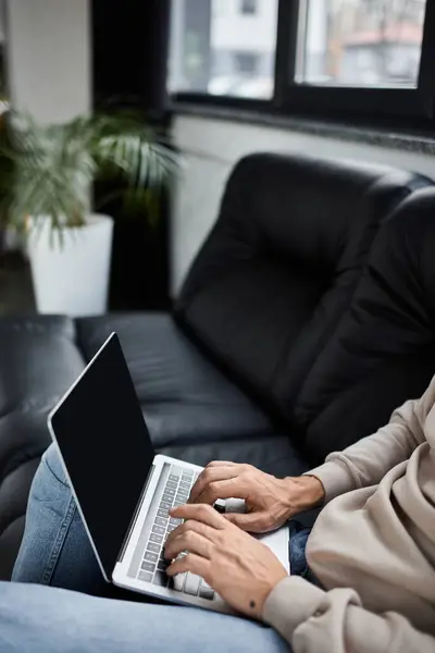 Individual types on a laptop while seated comfortably in a chic office space surrounded by plants. — Stock Photo