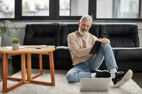 Un professionista anziano si siede sul pavimento, utilizzando un tablet in un elegante spazio di lavoro. — Foto stock
