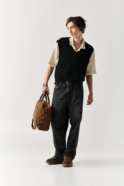 A confident young man poses with a fashionable outfit and a stylish bag in a minimalist studio. — Stock Photo