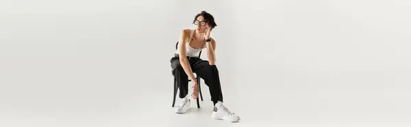 Um jovem magro em um top tanque branco senta-se graciosamente em uma cadeira em um estúdio, banner — Fotografia de Stock