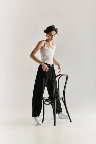 A slim young man in a white tank top shows off his style while engaging with a chair. — Stock Photo
