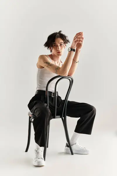 Un giovane elegante con una canotta bianca siede su una sedia, trasudando vibrazioni alla moda. — Foto stock