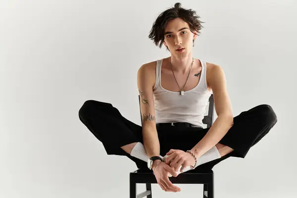Un joven delgado muestra su estilo con una camiseta blanca mientras está sentado con confianza. - foto de stock