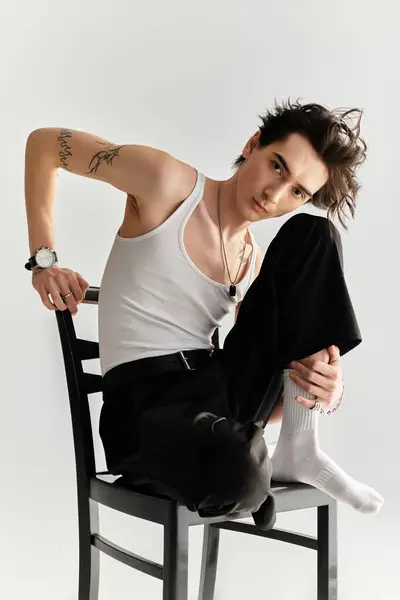 In a bright studio, a slim young man in a tank top poses confidently on a chair. — Stock Photo