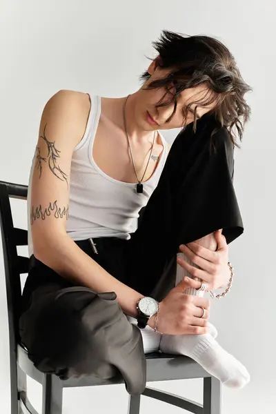 A young man in a white tank top poses relaxed in a chic studio showcasing his trendy style. — Stock Photo