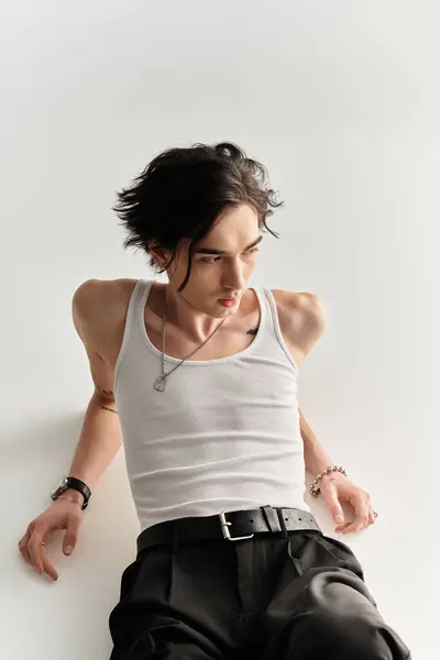 A slim young man in a white tank top poses stylishly in a bright studio, showcasing modern fashion. — Stock Photo