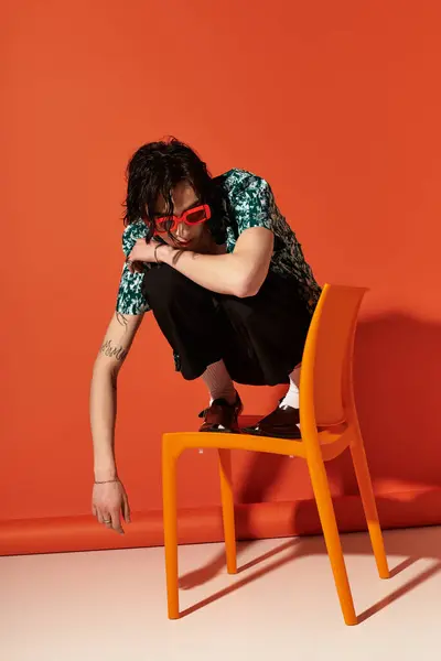 Young man showcases trendy summer fashion against a bold orange backdrop while seated. — Stock Photo
