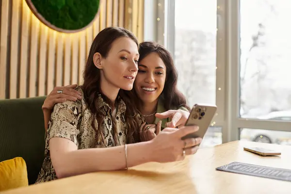 Two women share a moment of joy at a lively cafe, smiling as they enjoy digital content together. — Stock Photo