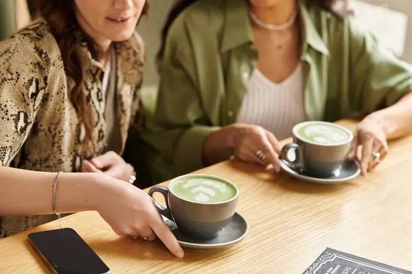 A lesbian couple shares joyful connection while sipping matcha at an inviting cafe. — Stock Photo