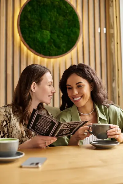 Two women enjoy each others company as they look at a menu while sipping coffee in a warm cafe — Stock Photo