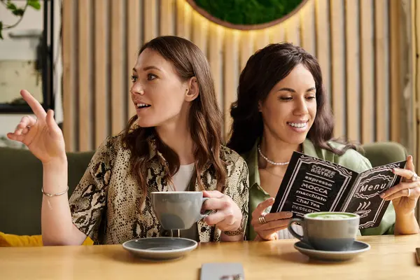 Two women share laughter and a warm connection while exploring the cafe menu over drinks. — Stock Photo