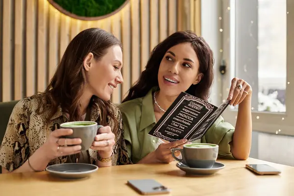 En un acogedor café, una pareja lesbiana bebe y navega juntos por el menú.. - foto de stock