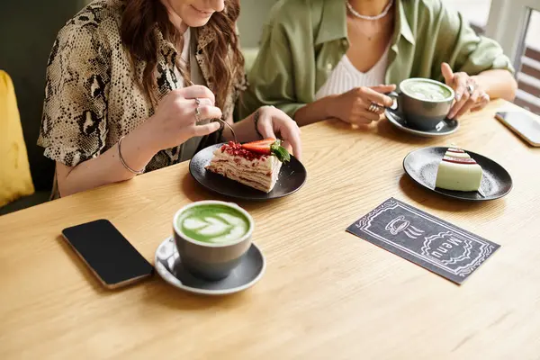 Two women savoring desserts and warm beverages, enjoying a delightful cafe atmosphere. — Stock Photo