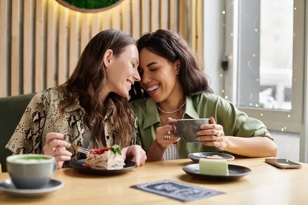 Two women enjoy each others company while savoring delicious desserts and drinks in a bright cafe. — Stock Photo