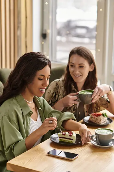 In a bright corner of a cafe, a happy lesbian couple shares delicious desserts while sipping drinks. — Stock Photo
