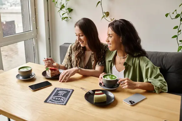 Two women enjoy delicious treats and warm beverages while sharing laughter at a cafe. — Stock Photo