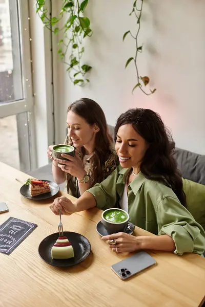 Two women enjoy each others company, sipping green tea and sharing desserts in a cafe. — Stock Photo