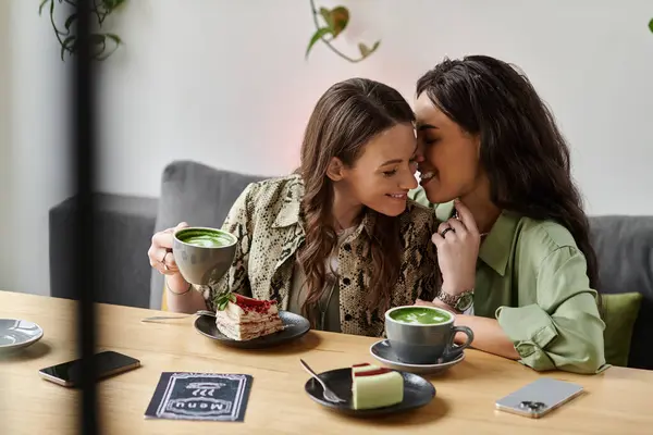 A joyful lesbian couple shares a sweet moment while enjoying matcha drinks and desserts. — Stock Photo