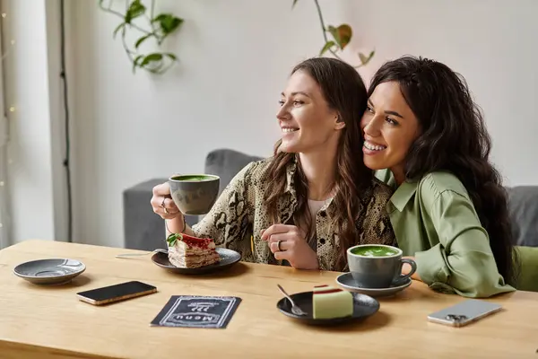 Two women sit together, smiling and enjoying drinks and dessert in a warm, inviting cafe. — Stock Photo