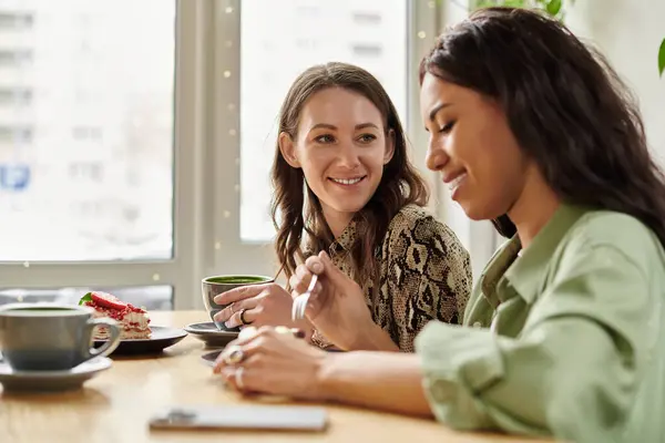 Two women share laughter and dessert while sipping drinks at a charming cafe, radiating joy. — Stock Photo