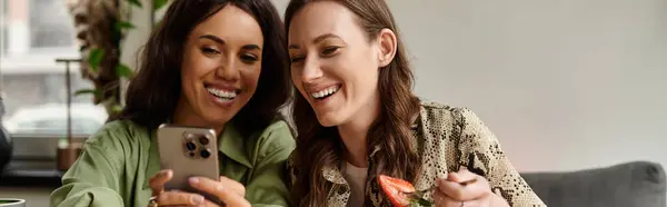 Two women share laughter and joy while looking at their phone at a cafe, surrounded by warmth. — Stock Photo