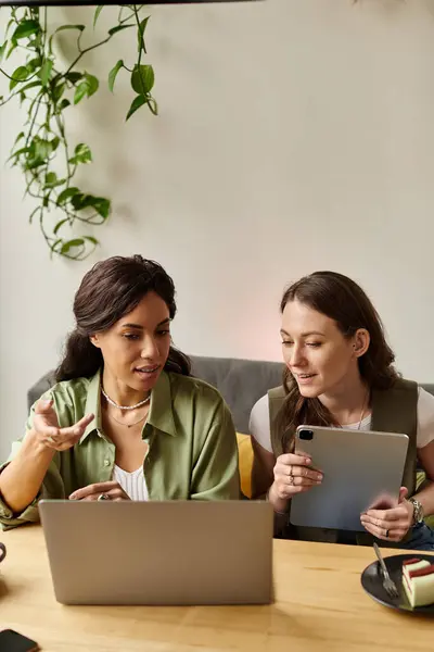 Two women engage in lively discussion at a cafe, sharing ideas over a laptop and tablet. — Stock Photo
