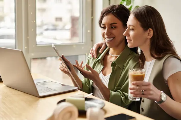 Two women share a joyful moment over drinks, engaged in a digital task at a cafe. — Stock Photo