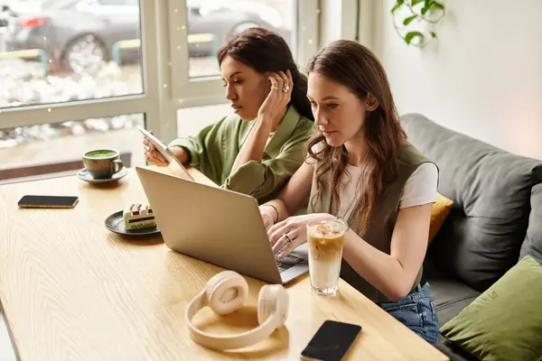 Two women enjoy an engaging moment at a cafe, focused on their laptops and phone, sharing ideas. — Stock Photo