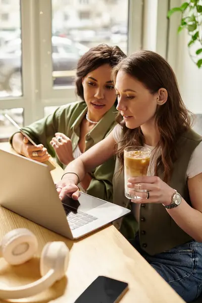 Two women share a delightful moment at a cafe, engaging in conversation while working on a laptop. — Stock Photo