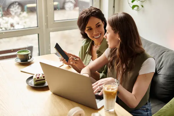 Two women share joy and conversation while working at a cafe table, surrounded by warm ambiance. — Stock Photo