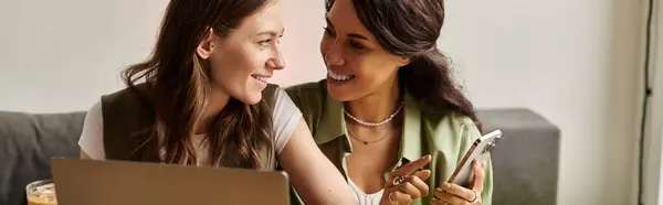 Sitting closely together, two women share smiles and laughter while using their devices at a cafe. — Stock Photo