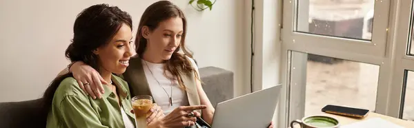 Two women sit together at a sunlit cafe, enjoying each others company and browsing a laptop. — Stock Photo