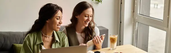 Two women share a joyful interaction over drinks and a smartphone at a cafe, radiating warmth. — Stock Photo