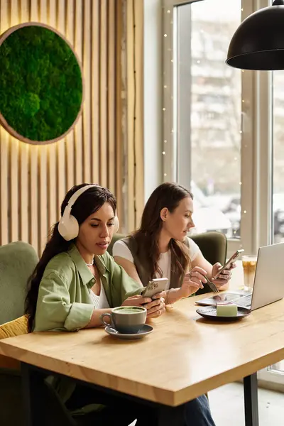 Inside a charming cafe, a lesbian couple relaxes at a wooden table, absorbed in their devices. — Stock Photo