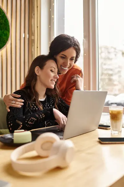 Two women share a joyful moment in a cafe, smiling and engaging with their laptops. — Stock Photo