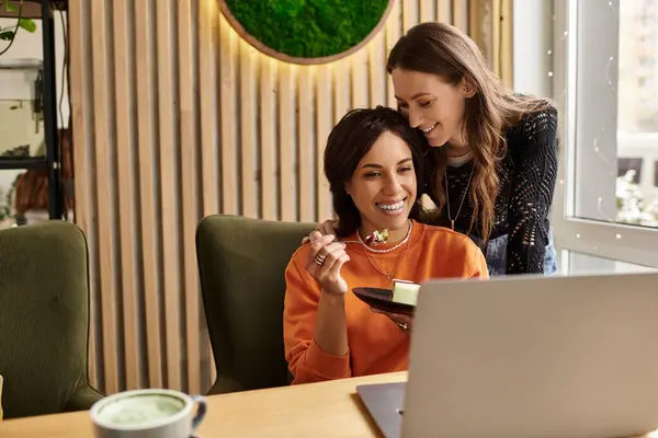 Zwei Frauen vergnügen sich in einem trendigen Café und teilen sich das Dessert, während sie am Laptop surfen. — Stockfoto