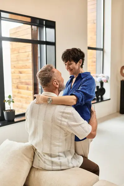 A joyful married couple shares a loving embrace in their stylish living area, radiating happiness. — Stock Photo