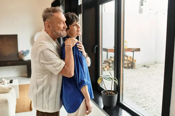 A joyful couple stands by the window, sharing a warm moment together, surrounded by home comfort. — Stock Photo